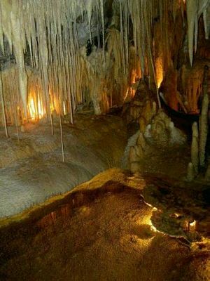 Spindles of white stalactite overhang a shelf of white limestone. The central floor is clear except for a thin stream of water.